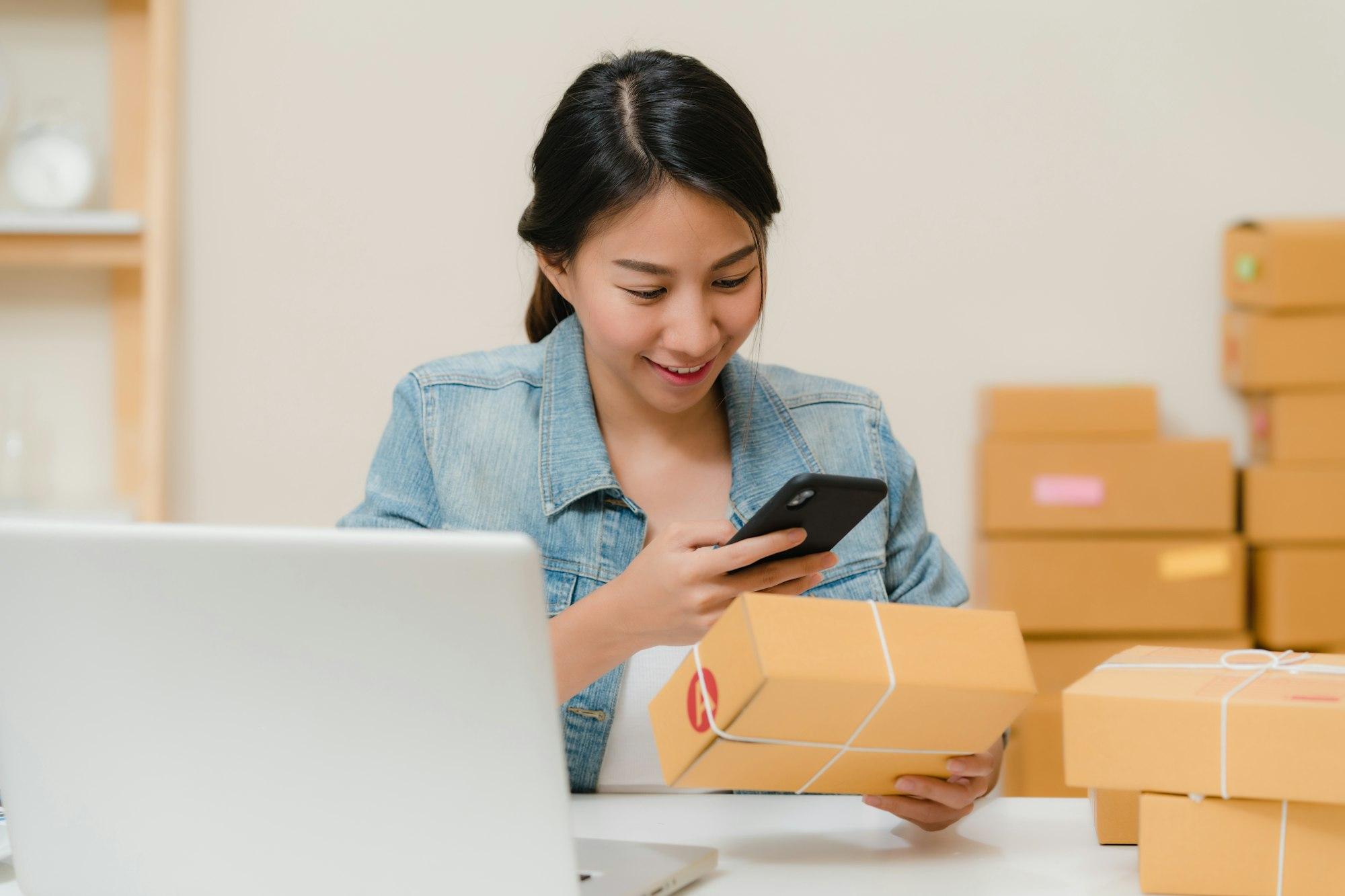 A woman checking a parcel on her phone beside a laptop