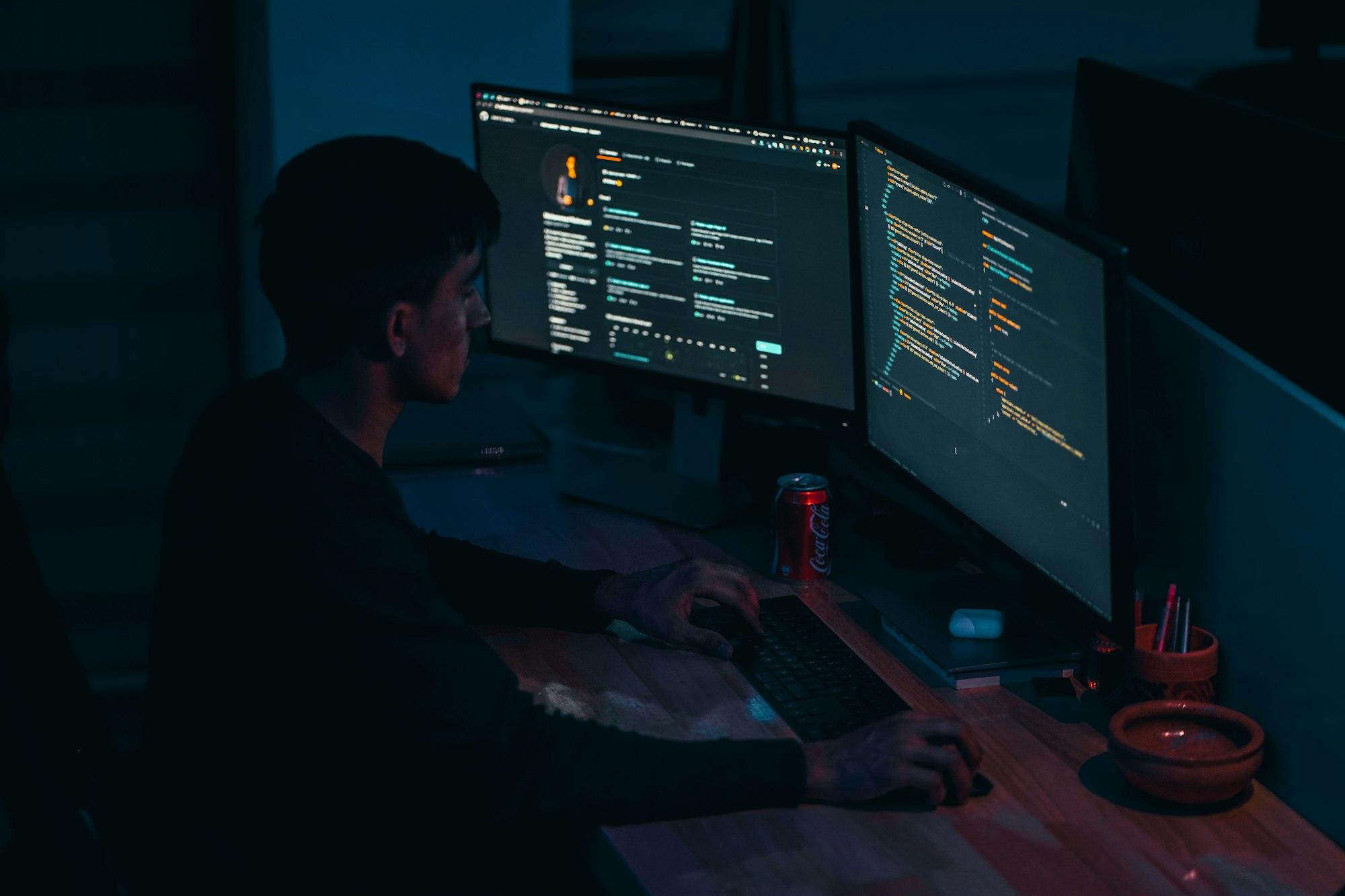 A developer working at monitors in a dark office