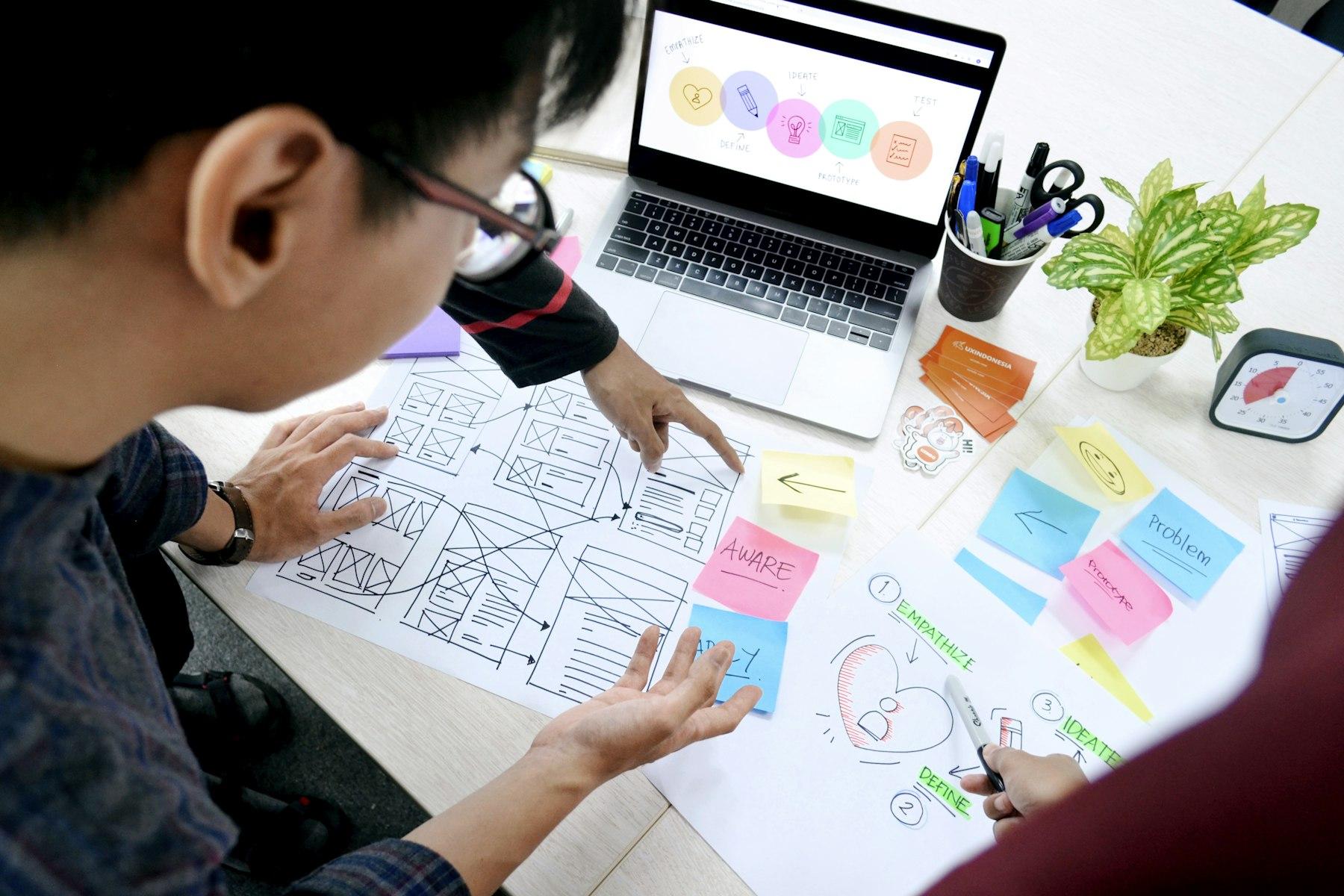 Designers sketching website wireframes beside a laptop